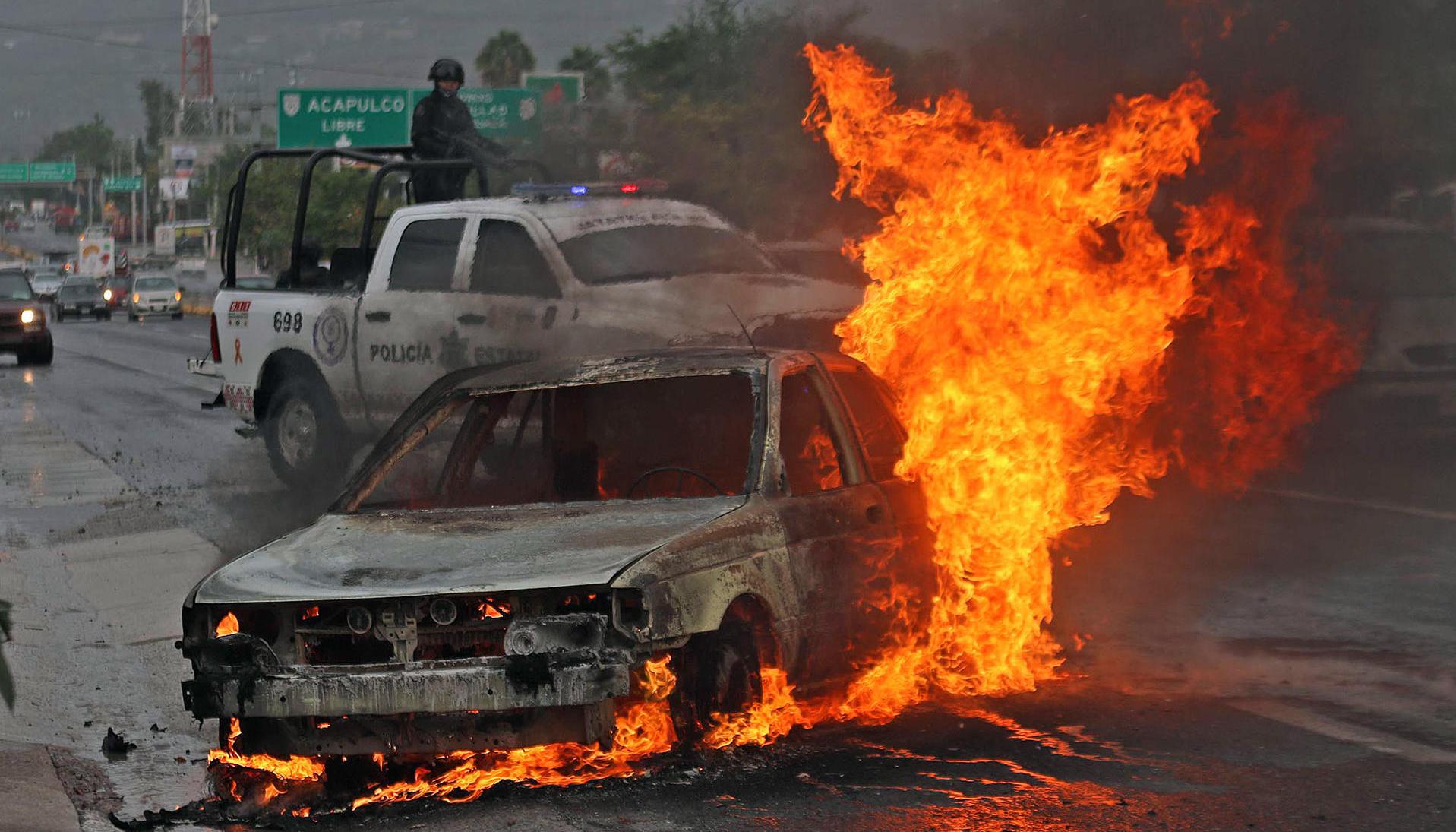 Personal de la policía estatal resguardan la zona donde un vehículo de alquiler fue incendiado. 