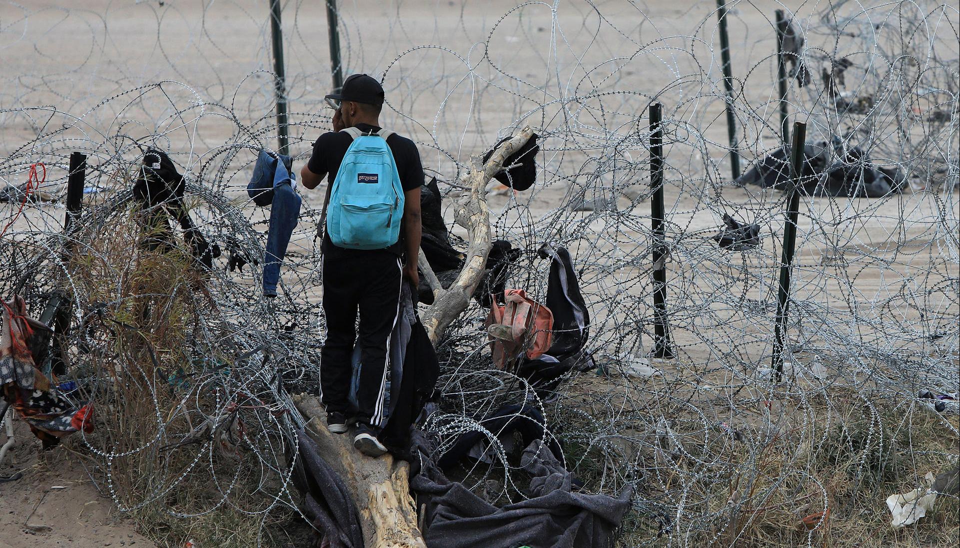 Migrantes buscan cruzar una alambrada en frontera entre México y EE.UU.