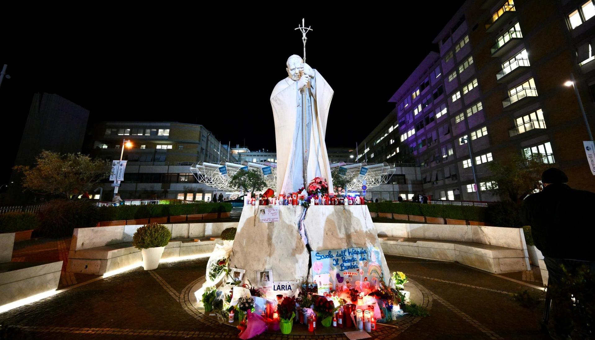 Flores y velas se encuentran a los pies de una estatua del Papa San Juan Pablo II fuera del Hospital Gemelli en Roma, Italia.