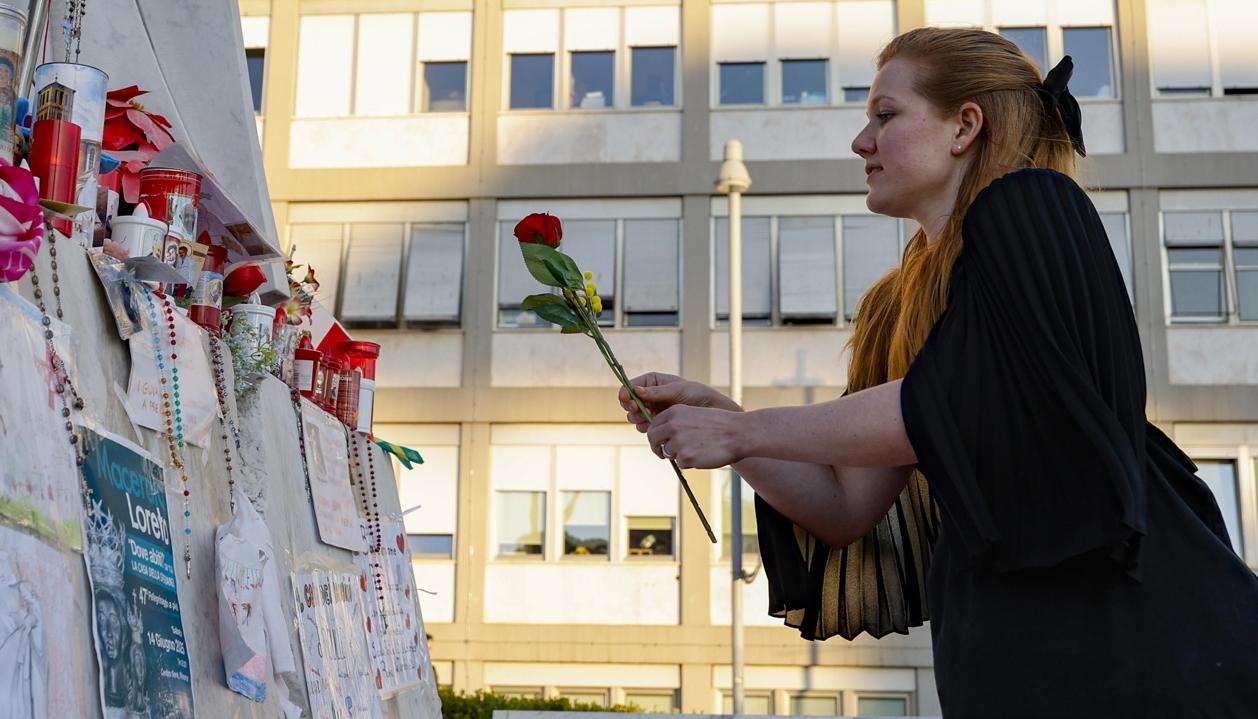 Una mujer coloca una flor frente a la estatua de Juan Pablo II en la entrada del Hospital Gemelli.