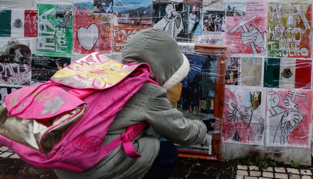 Un niño mira dibujos y fotografías colocadas en la parte inferior de la estatua de Juan Pablo II junto al Hospital Gemelli.
