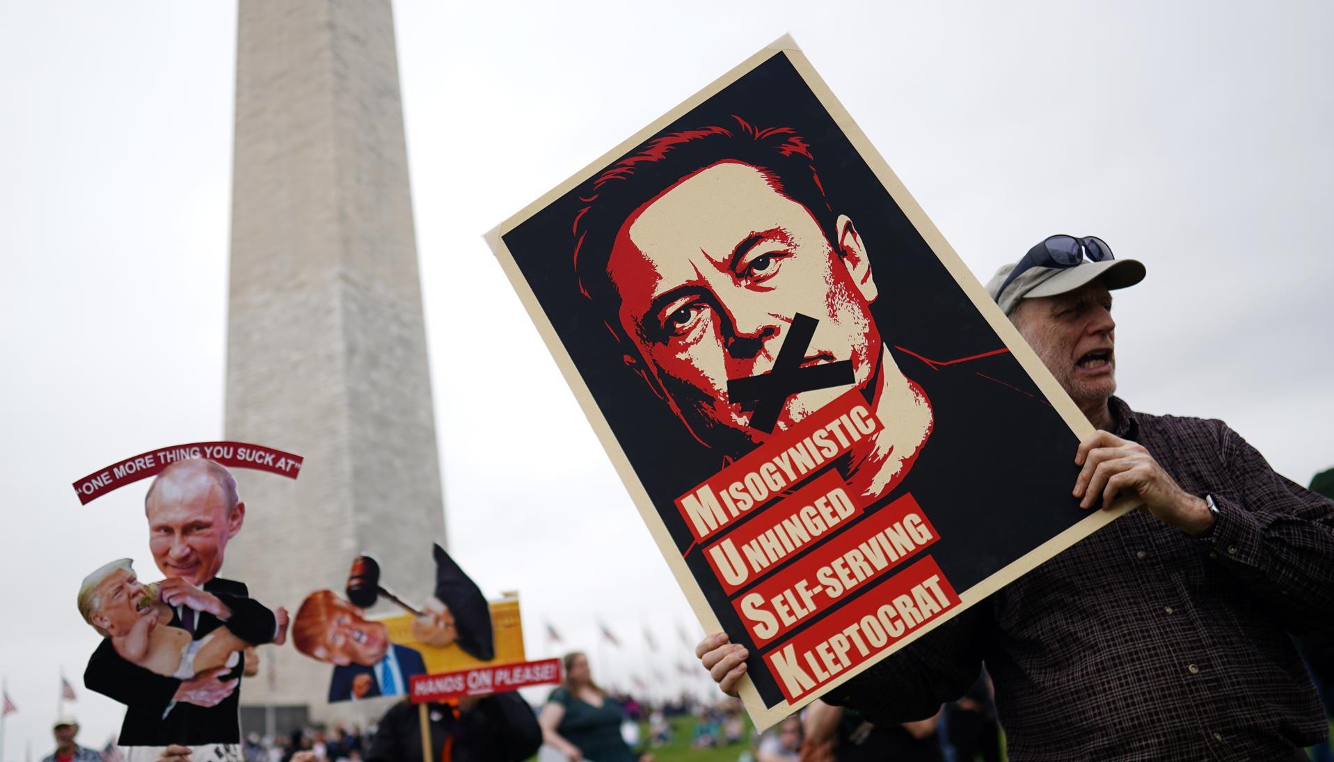 Un manifestante sostiene un cartel que representa a Elon Musk con el texto '¡Manos afuera!' en el National Mall en Washington.