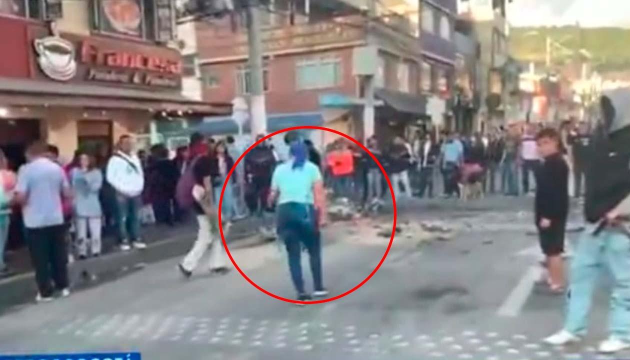 La mujer de azul y de espaldas, confrontado a los encapuchados