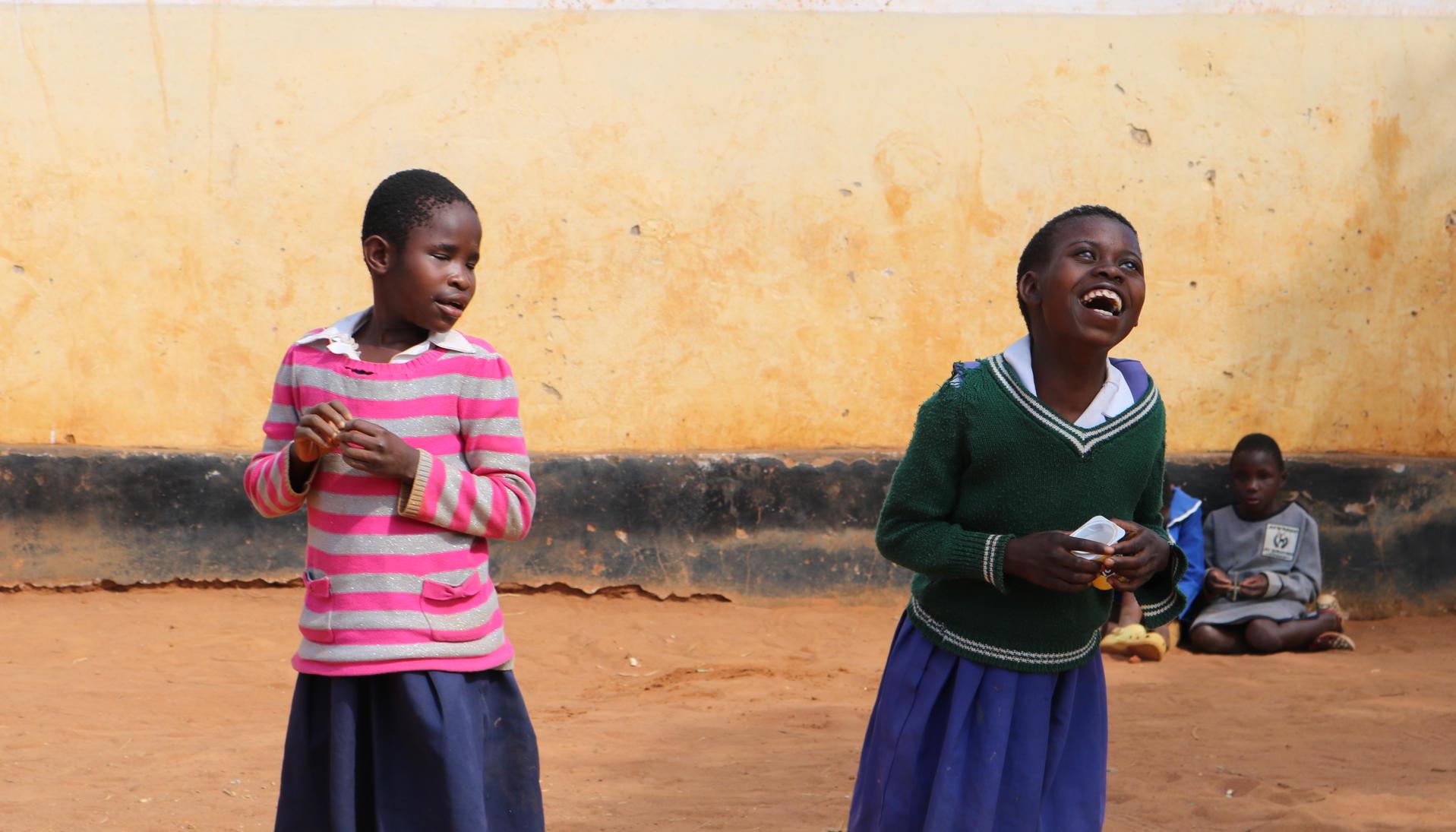 Dos estudiantes con discapacidad visual juegan y ríen durante el recreo.