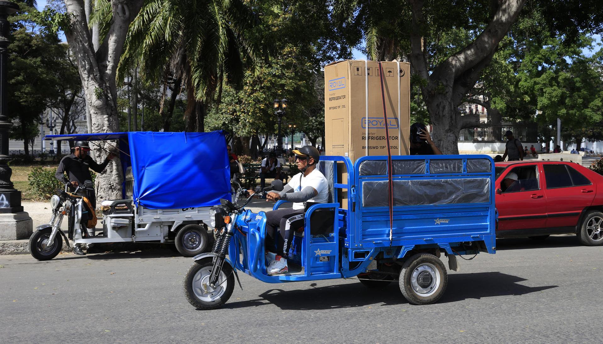 Una persona lleva un refrigerador en su triciclo en La Habana.