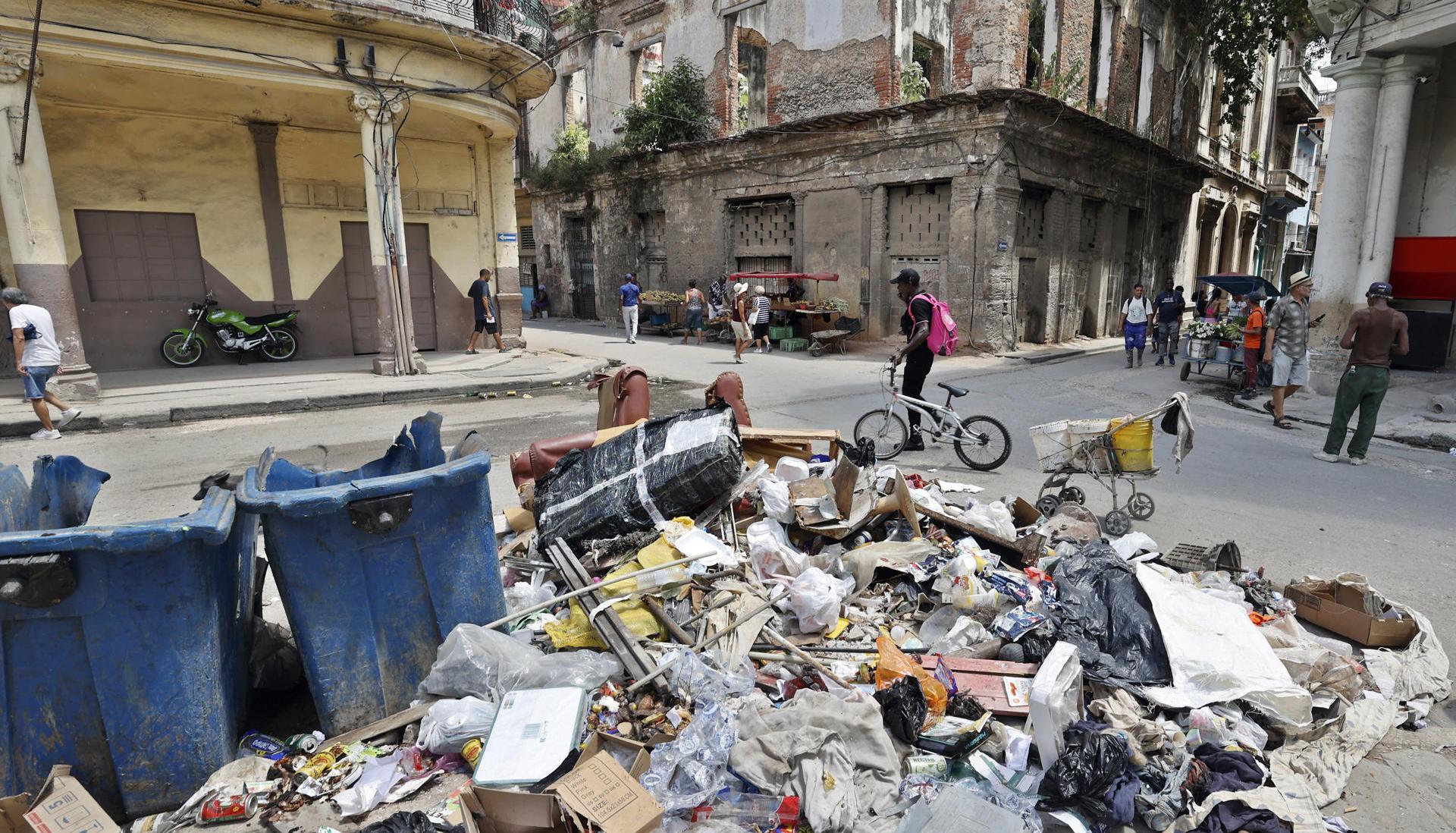 Personas caminan frente a basura acumulada por la falta de combustible para su recolección.