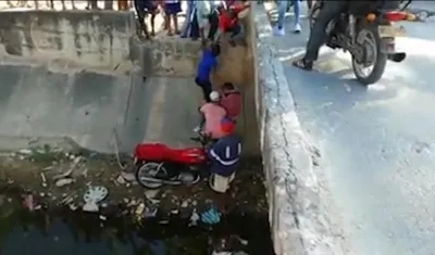 Momento en que vecinos ayudan a subir la moto donde se movilizaban padre e hijo.