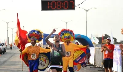 Gerard Giraldo cruza la meta escoltado por dos personajes carnavaleros. 