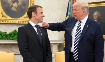 Donald Trump (derecha) le quita algo del hombro al presidente francés Emmanuel Macron.
