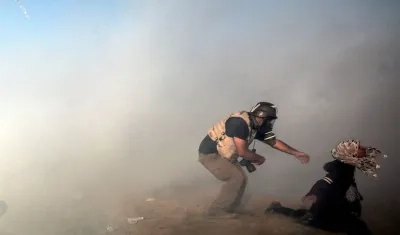 Un fotoperiodista trata de ayudar a una manifestante después de que los israelíes lanzaran gases lacrimógenos durante enfrentamientos registrados el pasado martes 15 de mayo, en la frontera con Israel, al este de la Franja de Gaza (Gaza). EFE