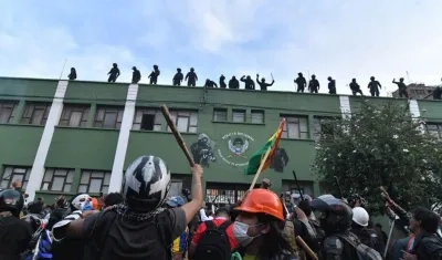 Policías bolivianos saludan desde el techo de una unidad policial a ciudadanos apostados en las puertas de la misma.