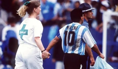 Diego Maradona sale de la mano con una voluntaria de la FIFA que lo conduce al examen antidoping. 