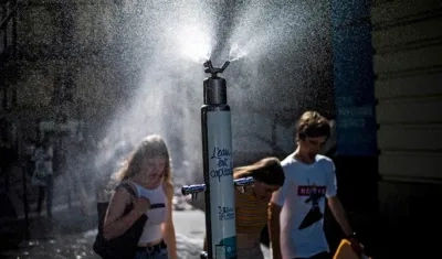  Varios transeúntes se refrescan con pulverizadores de agua públicos debido a las altas temperaturas.