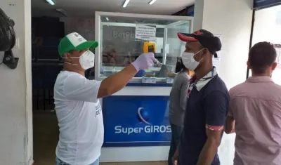 Un funcionario toma la temperatura a personas que se acercan a reclamar subsidios del adulto mayor en Soledad.