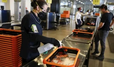 Una trabajadora desinfecta uno de los recipientes de objetos personales utilizados durante los controles de seguridad previos al abordaje, en el Aeropuerto Internacional El Dorado, en Bogotá.