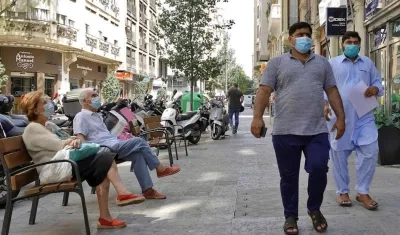 Dos personas descansan sentadas en un banco, mientras otras dos pasan a su lado, todas ellas con tapabocas.