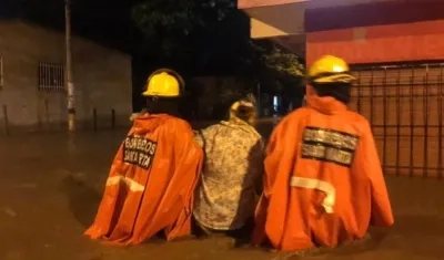 Dos bomberos conducen a una mujer en una calle totalmente inundada de Santa Marta.