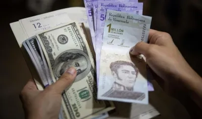 Una persona sostiene un fajo de billetes de dólares y bolívares.