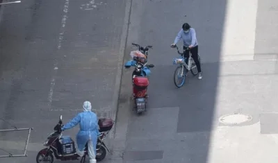 Un mensajero con equipo de protección personal y una mujer en bicicleta son vistos en Shanghai, China.