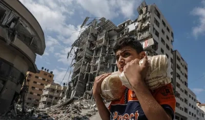 Un palestino lleva pan y al fondo se ven edificios destruidos en la ciudad de Gaza.
