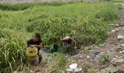 Dos personas sacando agua de un arroyo.