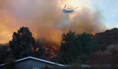 Un helicóptero arroja agua sobre una casa durante el incendio forestal en Los Ángeles.