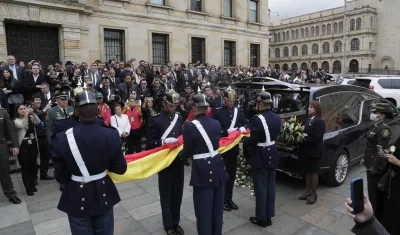 Integrantes del Batallón Guardia Presidencial doblan una bandera de Colombia junto a coche fúnebre con el féretro de Miguel Uribe.