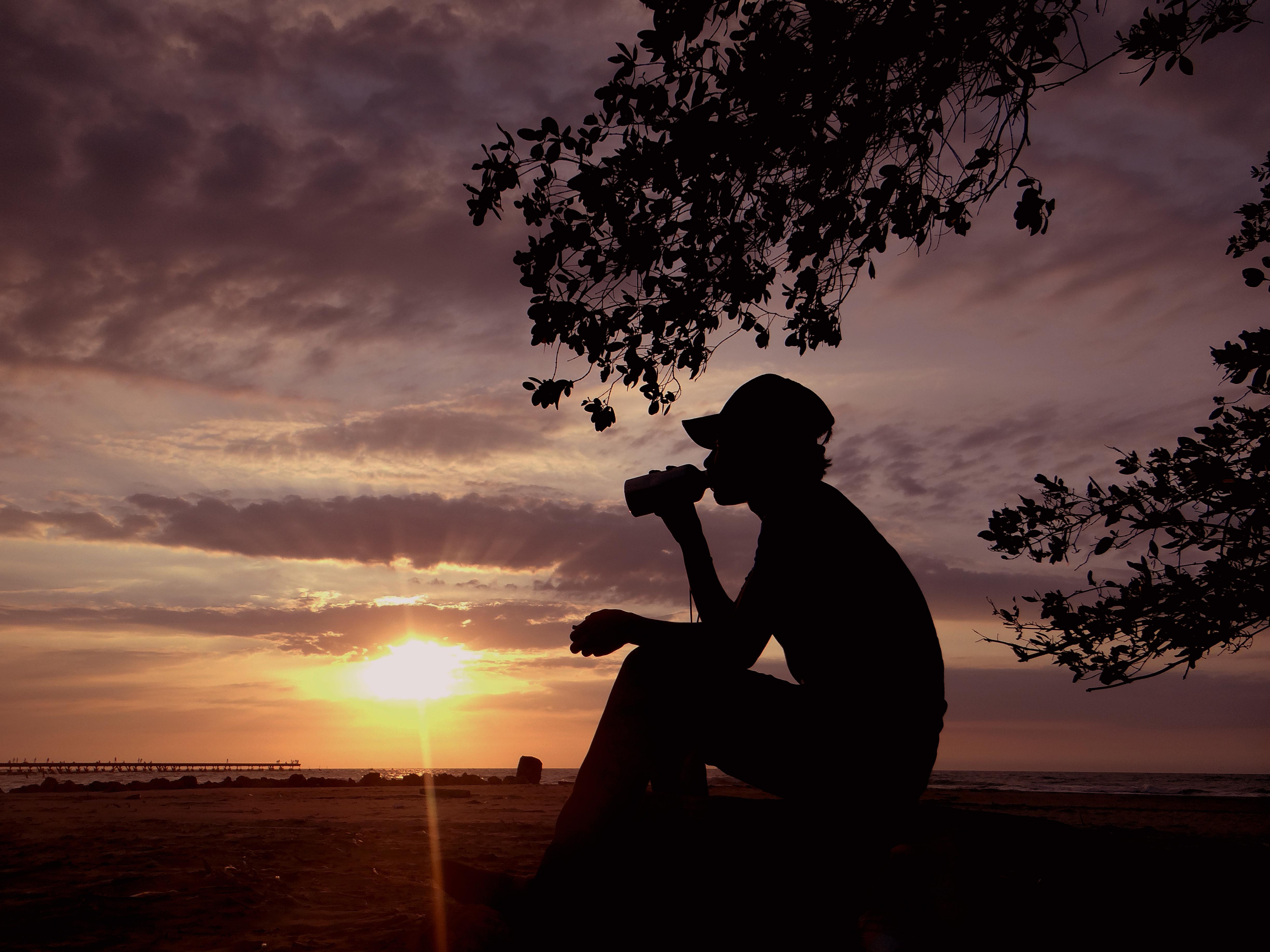 Puerto Colombia. Es una fotografía de un atardecer en las playas de Puerto Colombia donde una persona reposa, mientras toma un refresco contempla el bello horizonte.