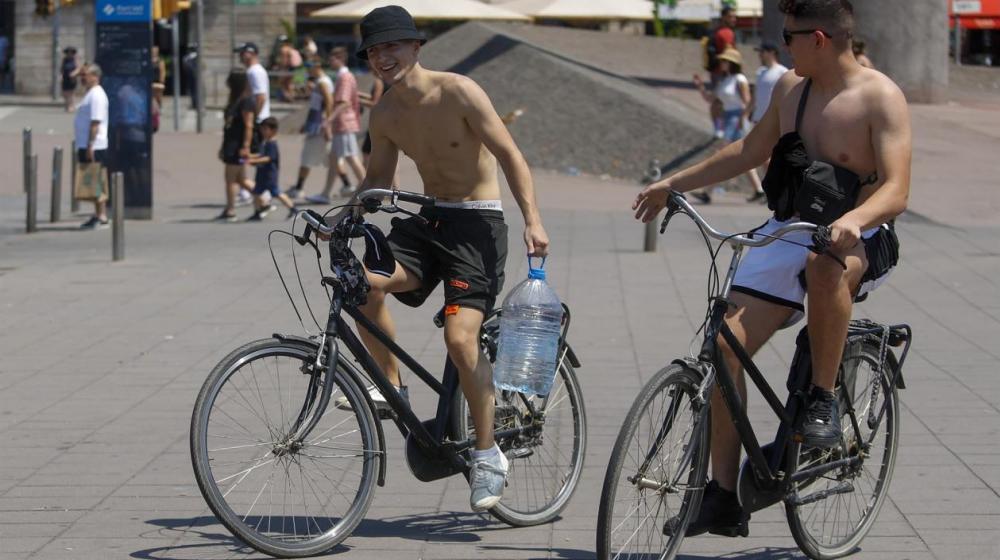 Unos turistas pasean con una garrafa de agua por el centro de Barcelona, que supera temperaturas de 41 grados.