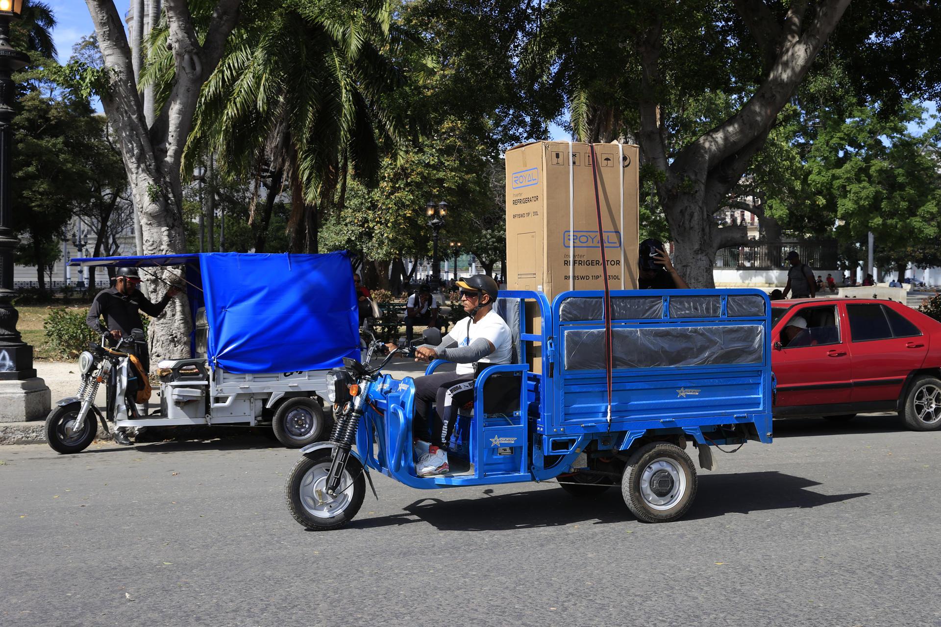 Una persona lleva un refrigerador en su triciclo en La Habana.